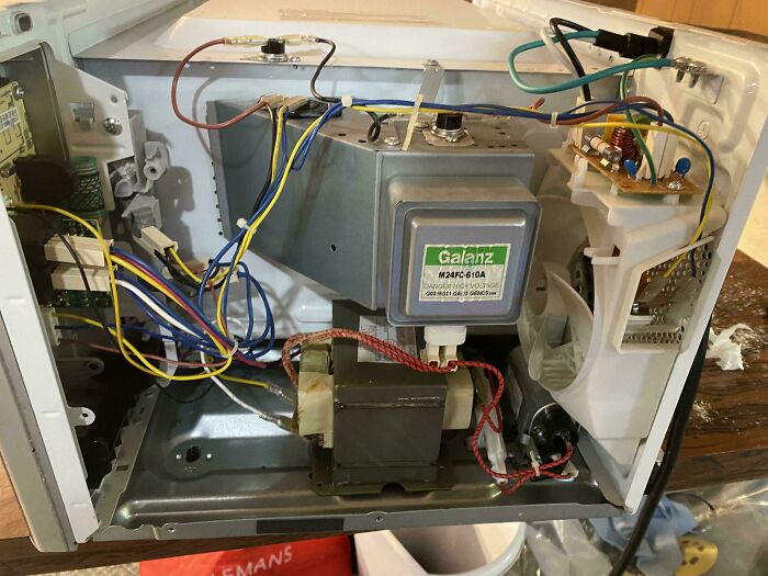 Opened microwave exposing complex internal wiring and components, illustrating dangerous things people did.