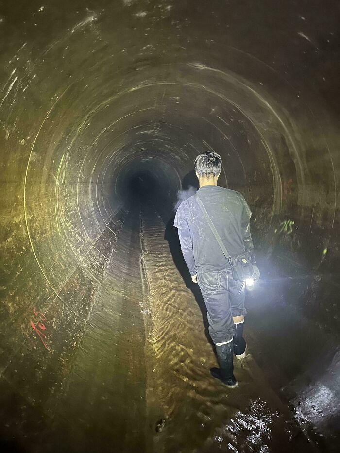 Man exploring a dark, water-filled tunnel with a flashlight, highlighting dangerous things people did.