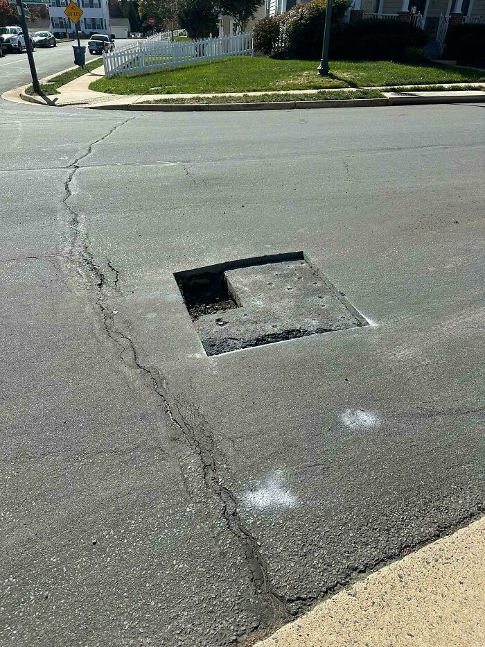 A square hole in the middle of a cracked asphalt road, showing a dangerous thing people did.