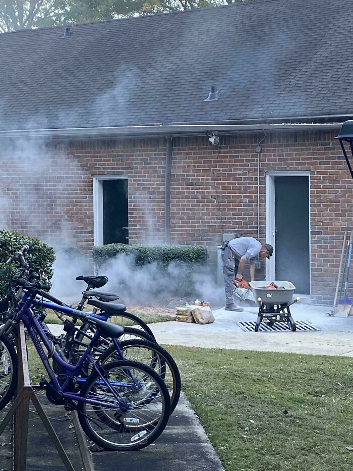 A construction worker creates smoke by cutting pavement near bicycles, a dangerous thing people did unnecessarily.