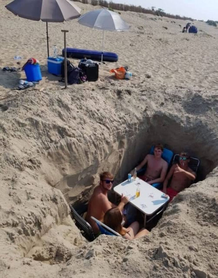 Three people sitting in a deeply dug, dangerous sand pit at the beach, an unnecessary risk.