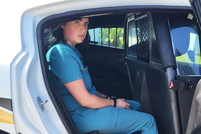 A woman in teal scrubs handcuffed in the back of a police car, a fascinating pic and quick fact.