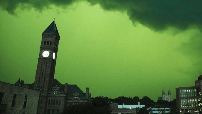 A fascinating pic of a city skyline with a tall clock tower under a vibrant green sky, a quick fact on weather.