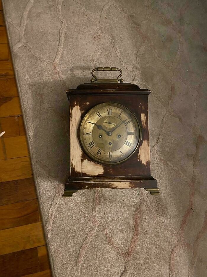 A remarkable antique mantel clock with a brass face and Roman numerals, showing distressed wood on a rug.