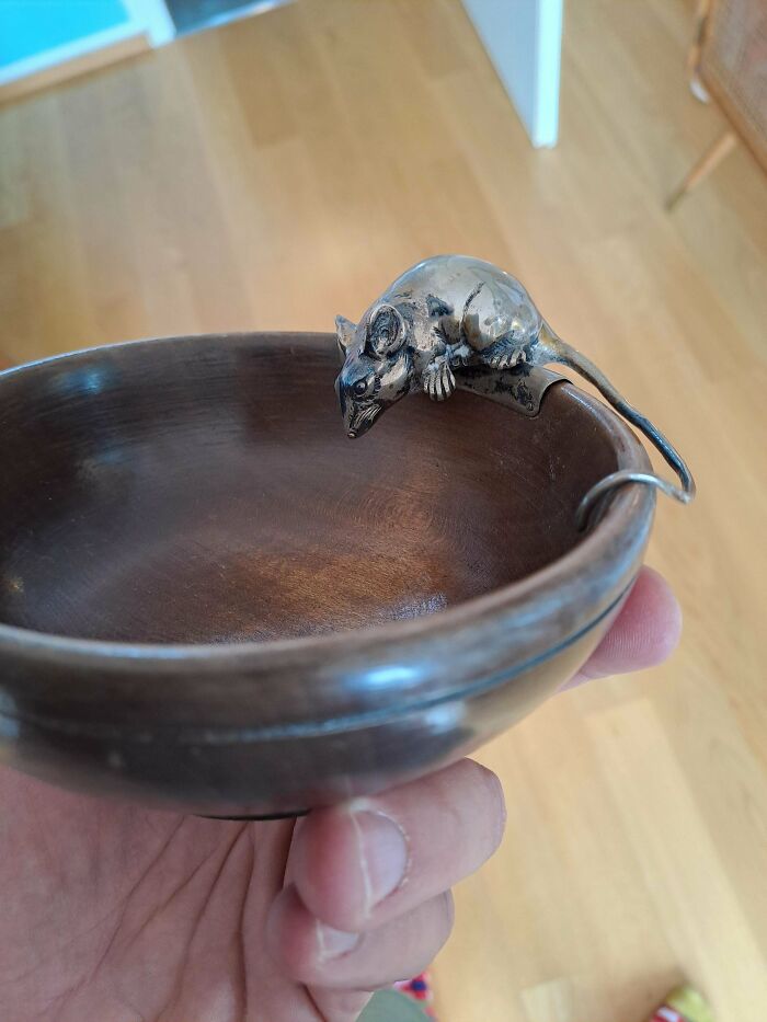 A hand holding a wooden bowl with a remarkable antique silver mouse perched on the rim.