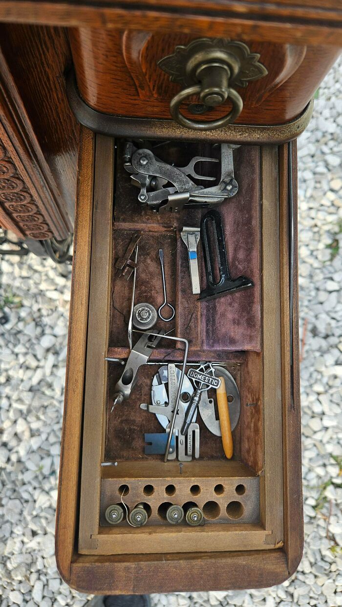 A wooden drawer from an antique sewing machine, filled with various vintage tools and accessories, remarkable antiques.