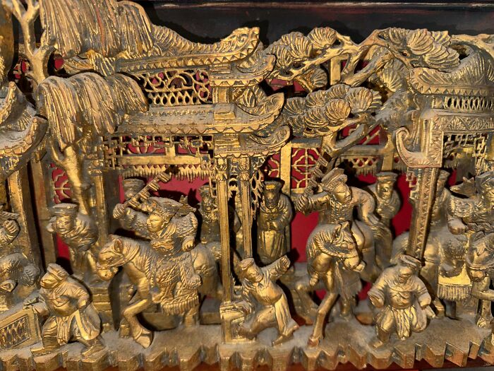 A close-up of an intricate, gold-colored carved wooden panel depicting a historical scene, remarkable antiques.