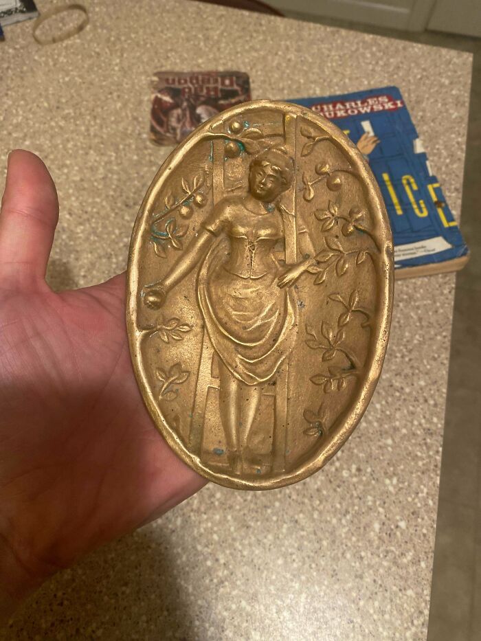 A hand holding a remarkable oval-shaped antique brass plaque featuring a relief of a woman, a special find.
