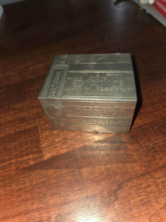 A remarkable antique metal box, intricately engraved with Russian text and designs, resting on a wooden surface.