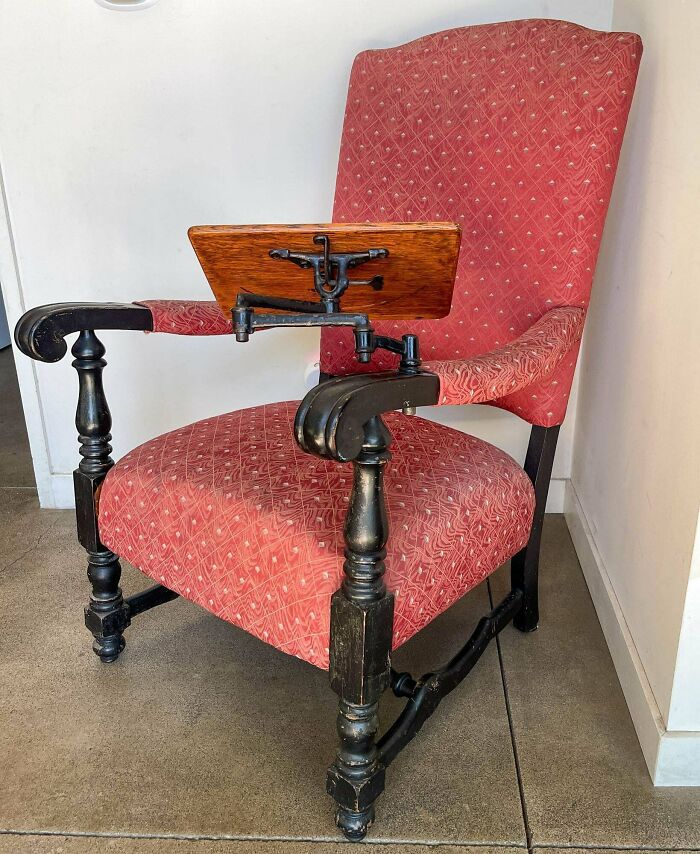 A remarkable antique chair with a red patterned upholstery and a wooden writing arm.
