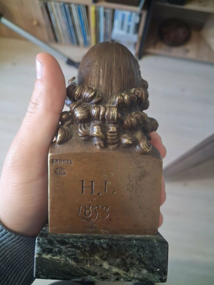 A hand holding a remarkable antique small bronze bust on a marble base, showing the inscription H.L. 1853.