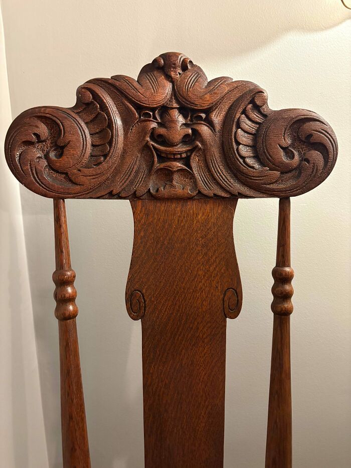 Close-up of the remarkable antique wooden chair back with an intricately carved face, showing detailed craftsmanship.