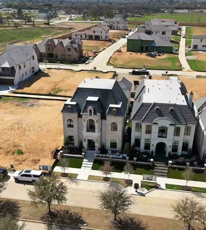Two newly built, large mansion-inspired houses in a developing suburban neighborhood, surrounded by dirt lots.