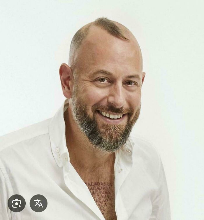 A smiling man with a beard and a small, spiky mohawk, showcasing a unique bad hair day.