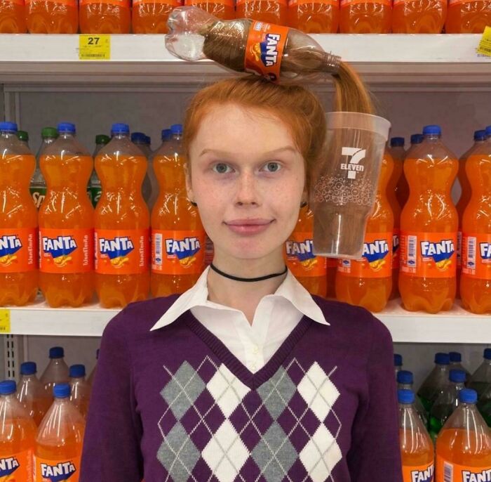 A red-haired woman with a Fanta bottle and 7-Eleven cup spilling hair, creating a bad hair day.
