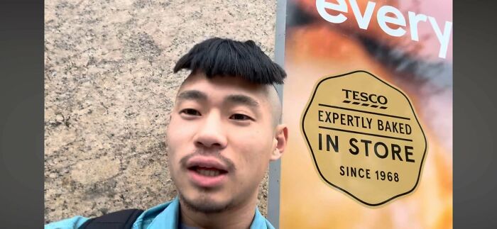 A man with a comical bad hair day, featuring an exaggerated, short fringe and shaved sides, standing near a store sign.