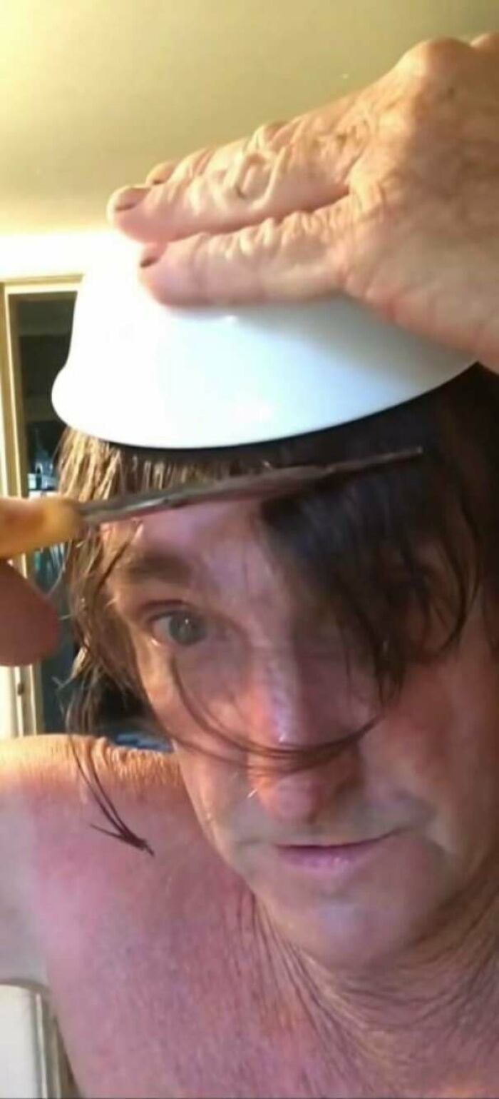 A person giving themselves a bad hair day with a bowl cut, holding a bowl on their head while cutting bangs.