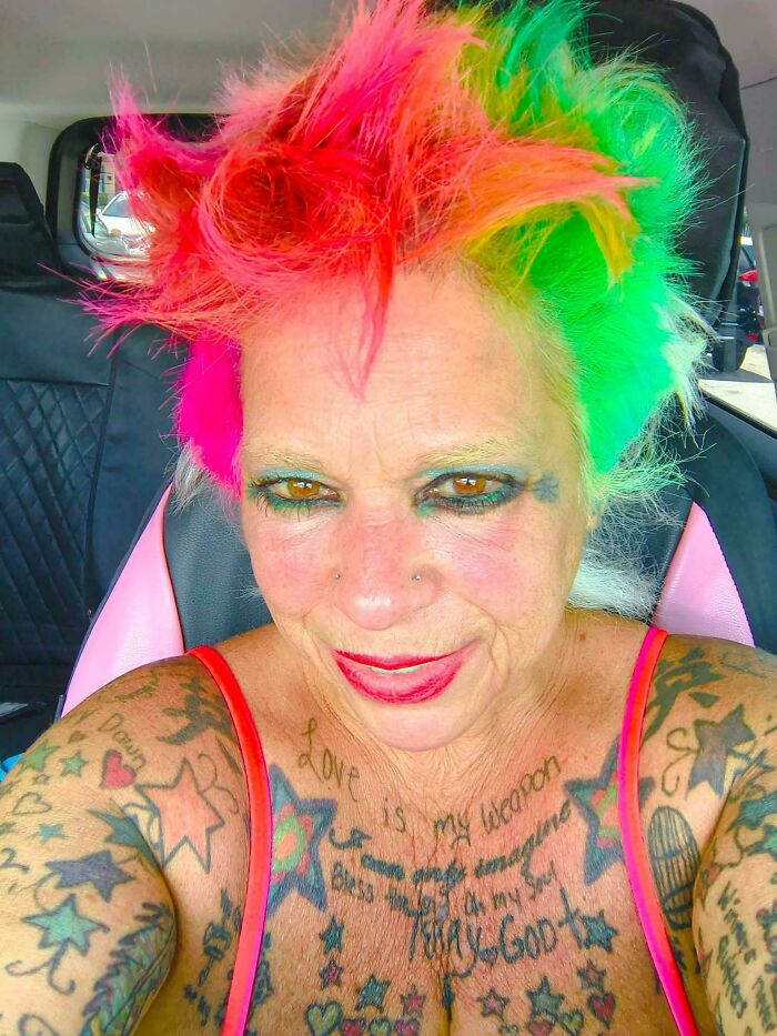 A woman with vibrant rainbow-colored bad hair day and numerous tattoos, looking directly at the camera.