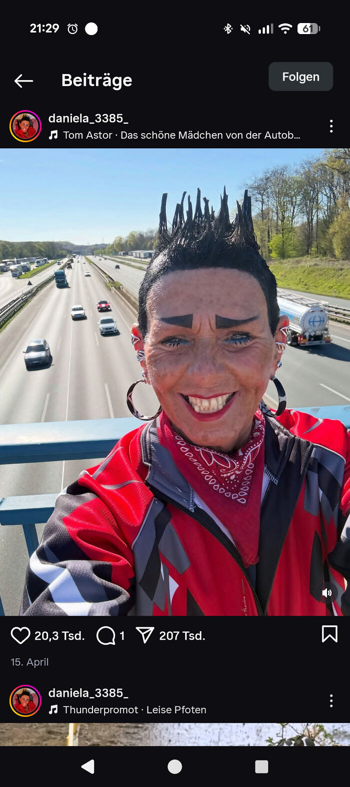 A person with a spiky bad hair day, smiling broadly on a bridge over a highway.