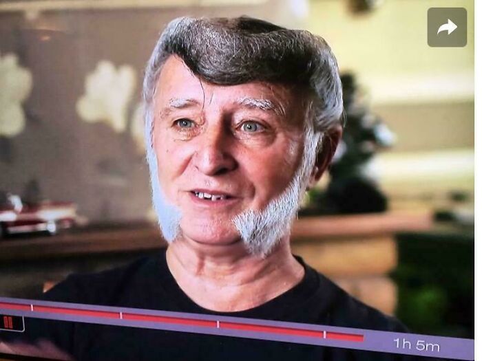 An older man with a bad hair day, sporting a grey pompadour and sideburns that are white.