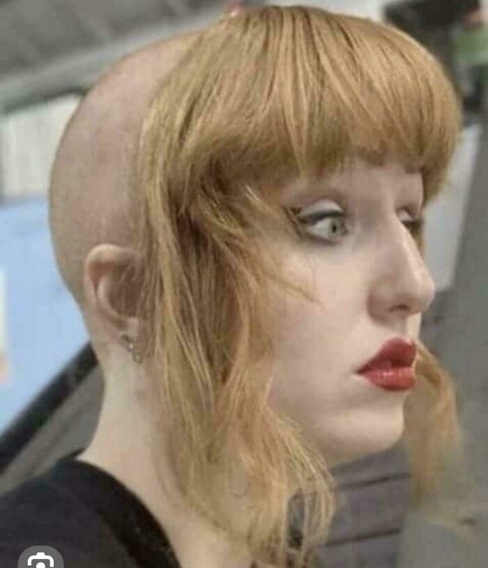A woman with a dramatically bad hair day, partially bald with long bangs and red lipstick, looks surprised.