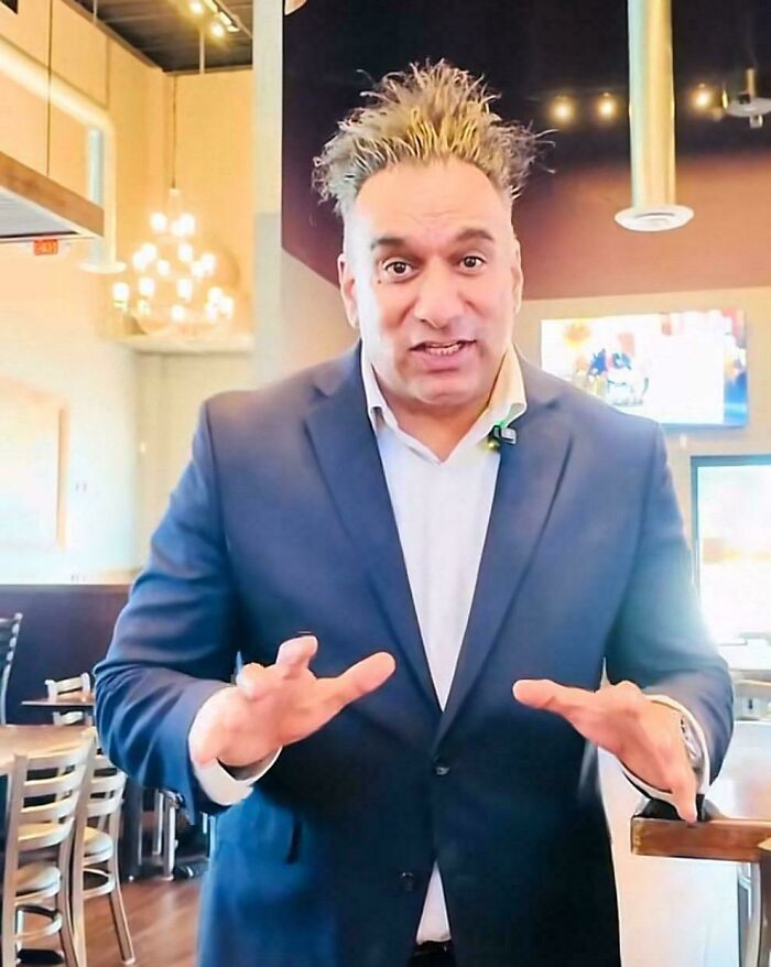 A man with a shocking bad hair day, standing in a restaurant with his spiky hair.