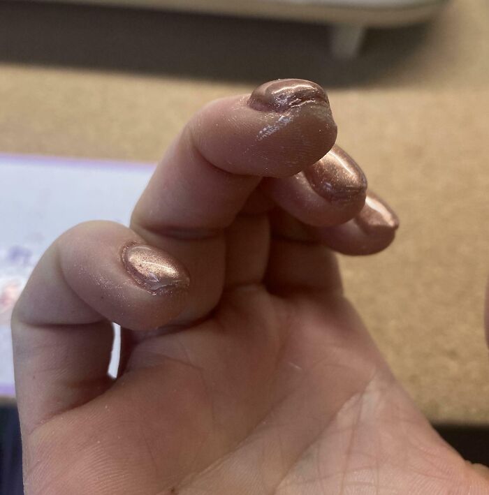A hand with poorly applied, chipped rose gold nail polish, a beauty salon mishap looking significantly worse.
