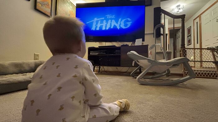 A baby sitting on a rug watching a movie on a TV, highlighting the wholesome and fun side of being a dad.