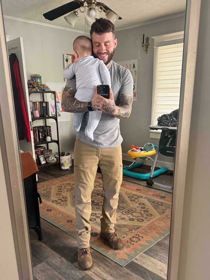 A tattooed dad holding his baby in a mirror selfie, showing the wholesome side of being a dad.