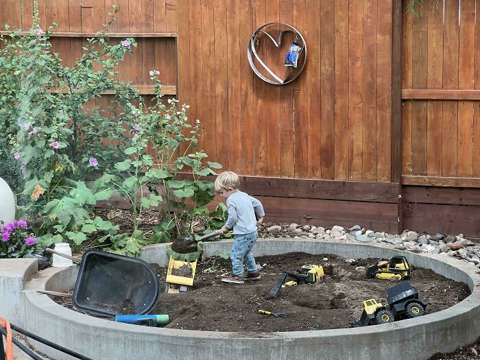 A young boy playing in a sandbox with toy construction vehicles, a wholesome and fun side of being a dad.