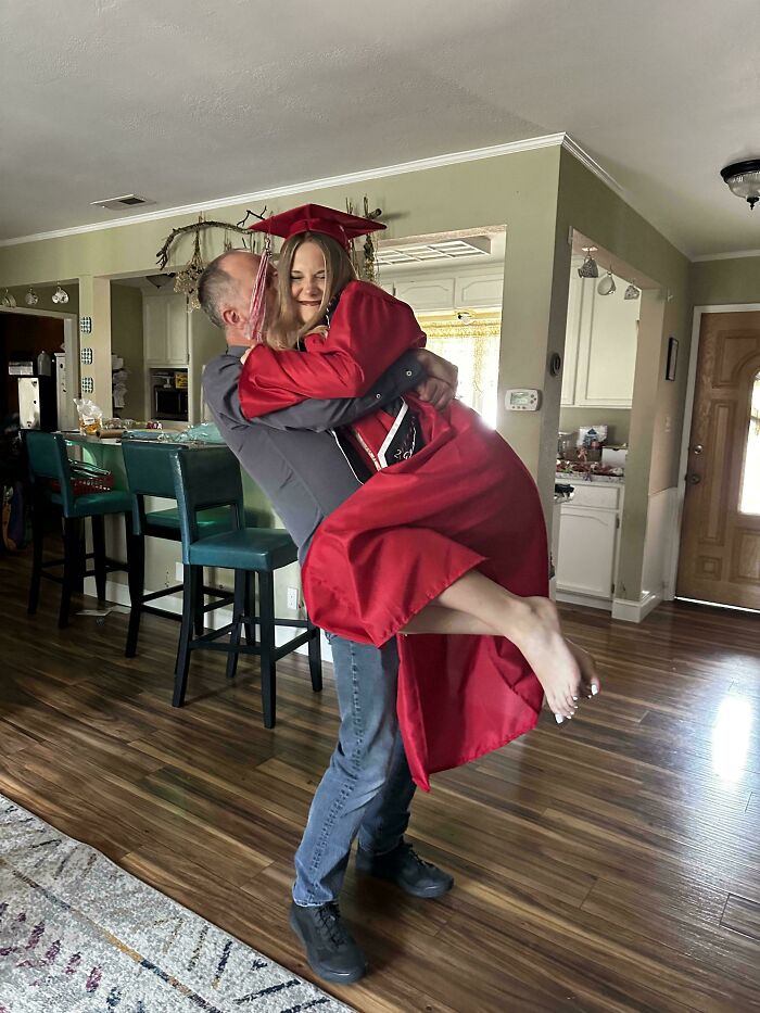 A dad happily holding his daughter in a red graduation gown, celebrating the wholesome and fun side of being a dad.