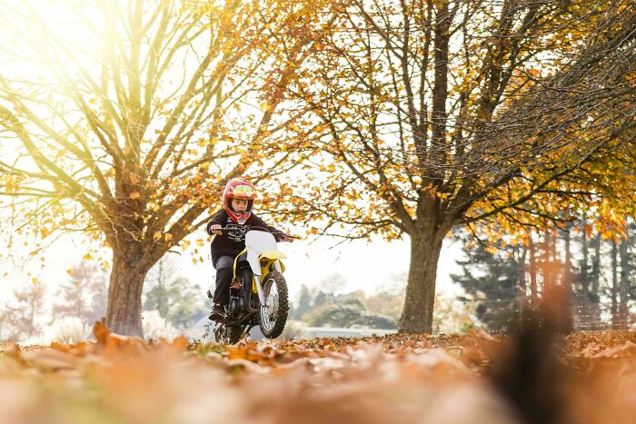 A young boy riding a dirt bike through a park with autumn leaves, highlighting the wholesome and fun side of being a dad.