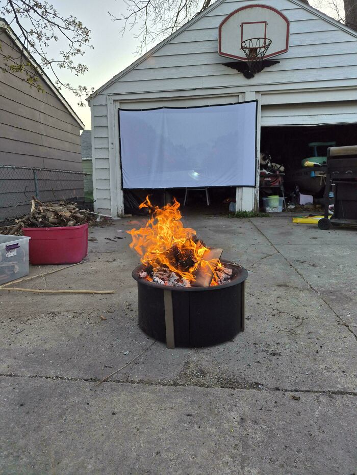 A fire pit burning brightly in a driveway, with a projector screen set up, illustrating the wholesome and fun side of being a dad.