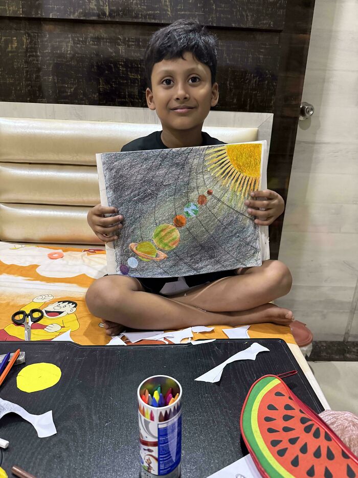 A young boy proudly holding up his drawing of the solar system, reflecting the wholesome and fun side of being a dad.