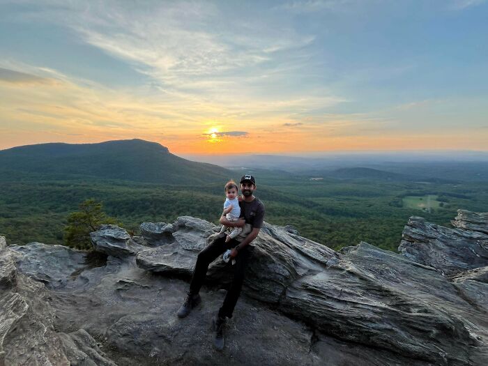 Dad holding baby on a mountaintop at sunset, capturing the wholesome and fun side of being a dad.