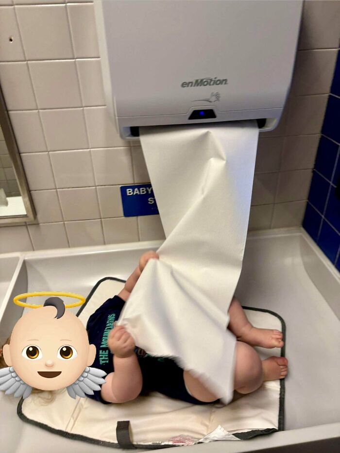Baby on changing table pulling paper from dispenser, a wholesome and fun dad moment.