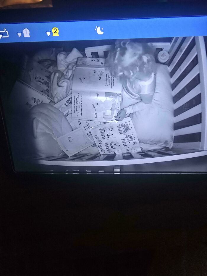 Baby in crib, surrounded by books, captured by a baby cam, showing the fun side of being a dad.