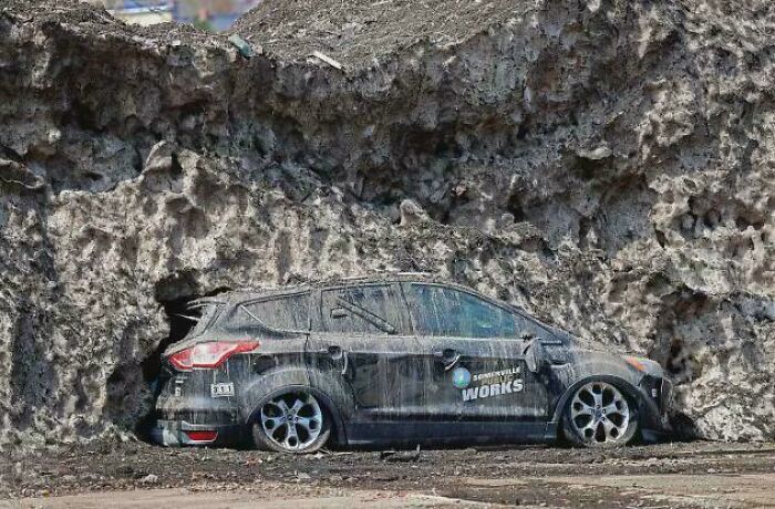 A black car partially buried under a large mound of dirt and debris, an interesting photo.