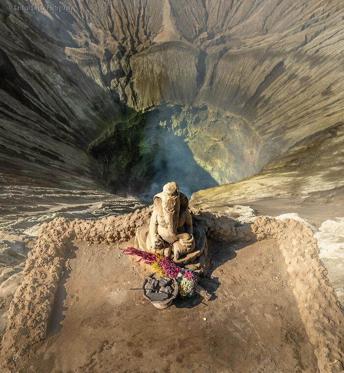 An interesting Ganesha statue with offerings overlooking the smoky, colorful crater of a volcano.