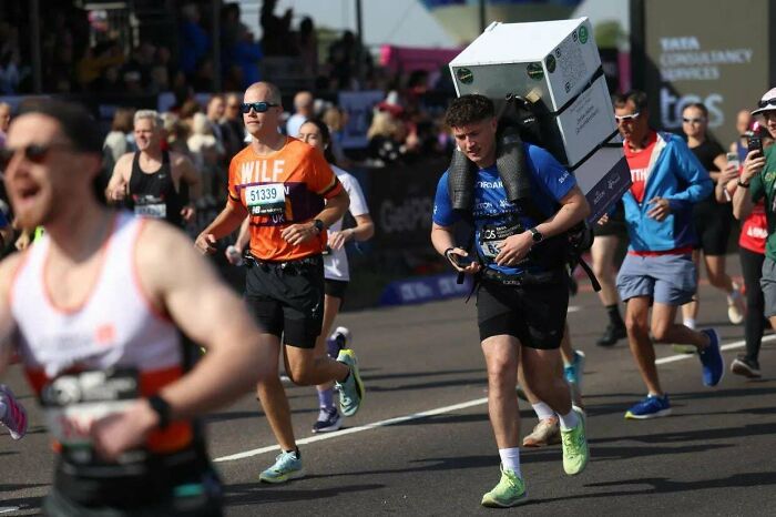 A man running in a marathon with an interesting large, rectangular object strapped to his back.
