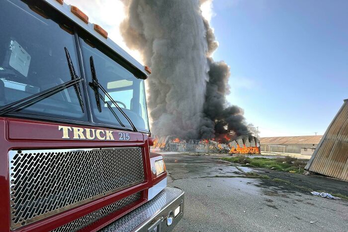 A massive fire producing thick smoke, with a red fire truck in the foreground, an interesting photo.