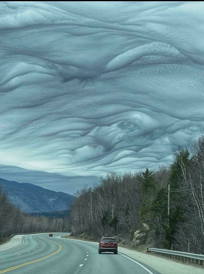An interesting landscape with a winding road under fascinating, wavy cloud formations in a mountain setting
