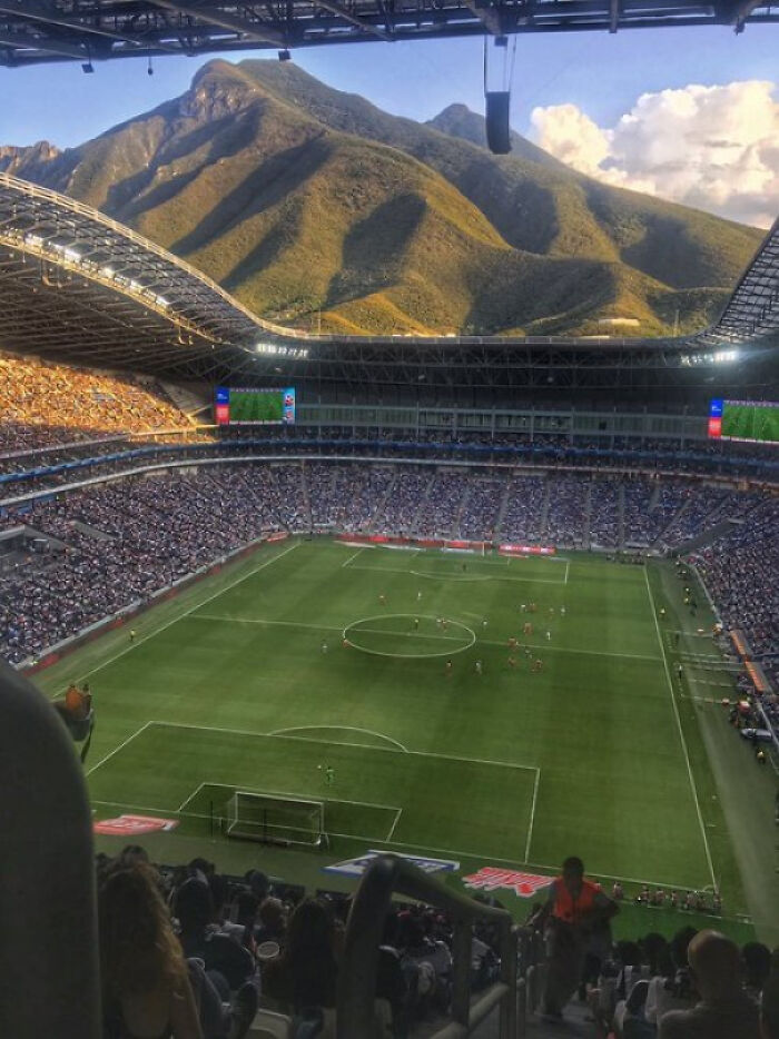 An interesting photo of a packed soccer stadium with a stunning mountain backdrop under a partly cloudy sky.