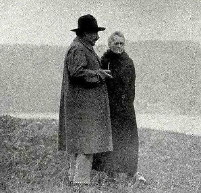 An interesting historical photo of Albert Einstein and Marie Curie standing in an open field.