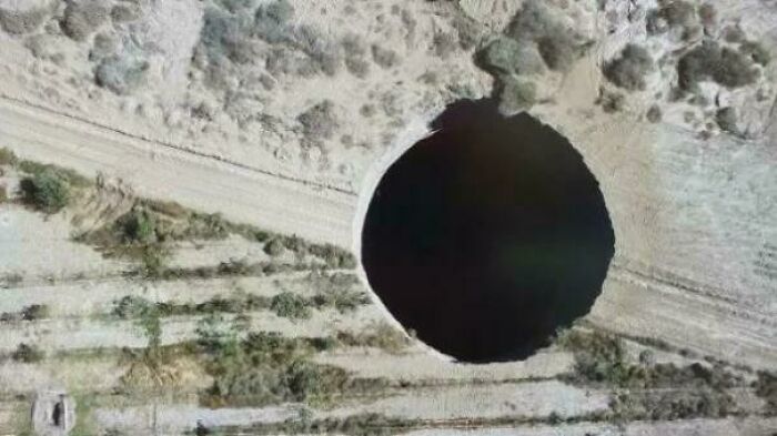 An interesting aerial photo of a perfectly circular, dark sinkhole in a dry, barren landscape.