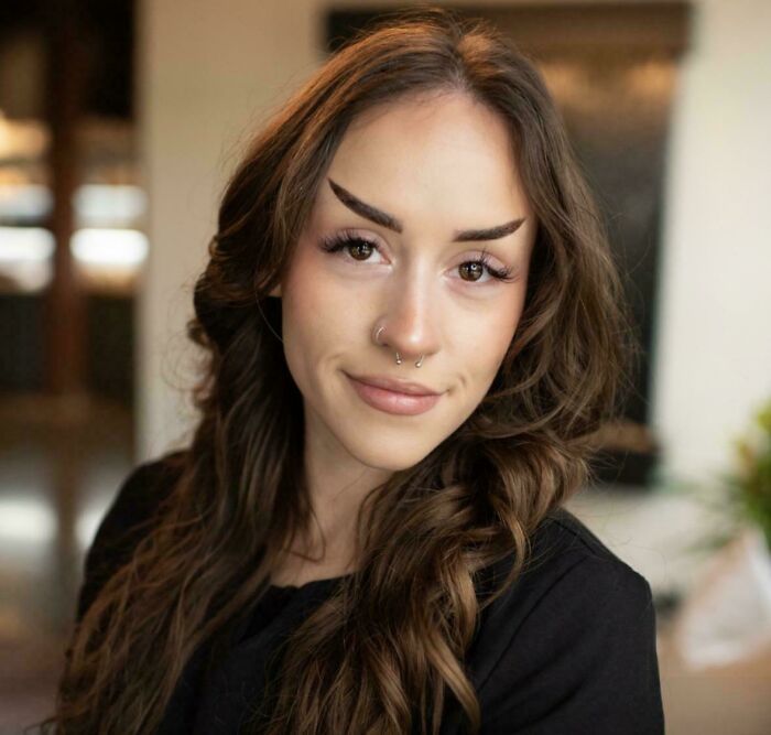 A young woman with long brown hair and unusually shaped, arched eyebrows, showcasing a beauty salon mishap.