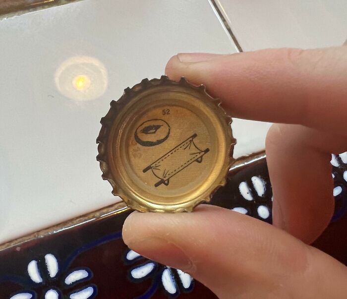 A hand holding a bottle cap with a small compass and a cot diagram inside, posing a visual brain puzzle.