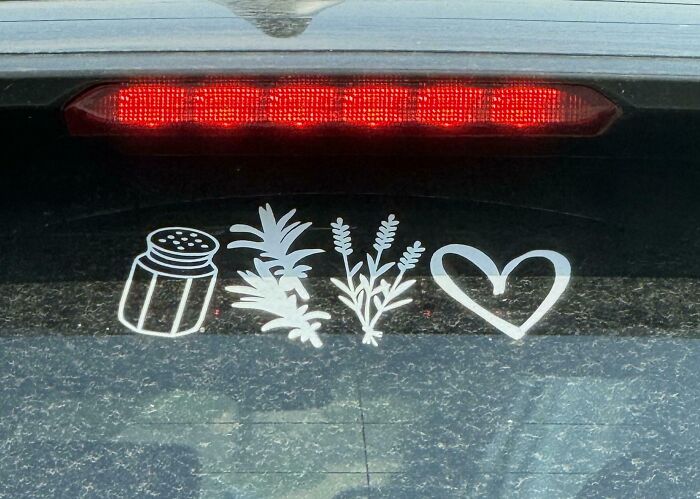 Four white vinyl decals on a car window: a salt shaker, two herb sprigs, and a heart, forming a brain puzzle.