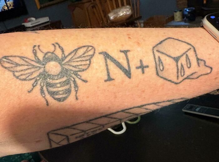 A tattoo on an arm, showing a bee, an N, and an ice cube, forming a clever brain puzzle.
