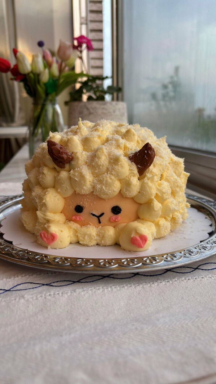 An adorable sheep-shaped cake with fluffy frosting, tiny ears, and a cute face, proving bakers make delicious treats.